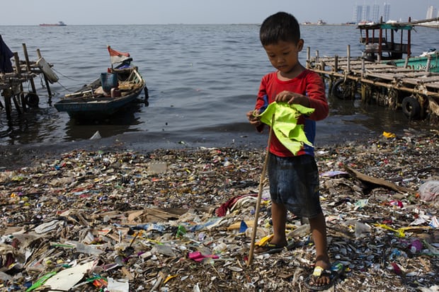 A boy plays with a makeshift flagpole on a beach covered in plastic waste in Indonesia. Photograph: Ed Wray/Getty Images