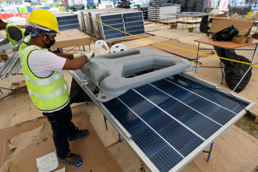 This photograph taken on February 3, 2021 shows a worker fixing a floater onto a solar panel as part of the construction of a floating solar power farm on Tengeh reservoir in Singapore. Thousands of panels glinting in the sun stretch into the sea off Singapore, part of the land-scarce city-state’s push to build floating solar farms to cut greenhouse gas emissions. (Photo by Roslan Rahman)