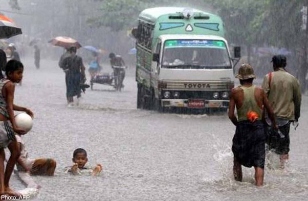 Myanmese children play along a flooded street as a vehicle make its way in Yangon