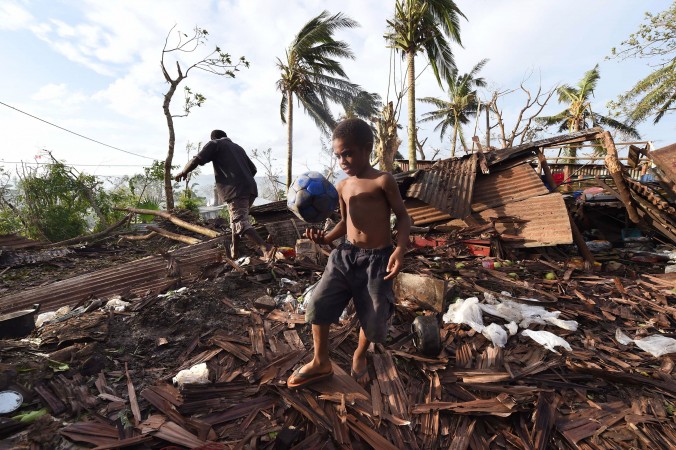 Samuel, only his first name given, carries a ball through the ruins of their family home as his father, Phillip (at the back), picks through the debris in Port Vila, Vanuatu in the aftermath of Cyclone Pam, March 16, 2015. (AP Photo/Dave Hunt)